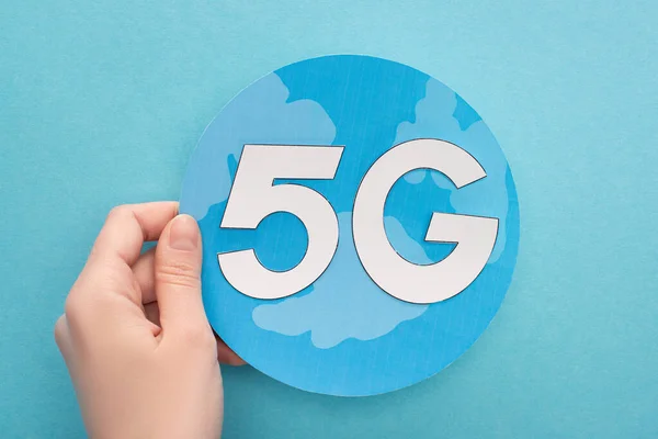 Cropped view of woman holding white 5g lettering on globe on blue background — Stock Photo