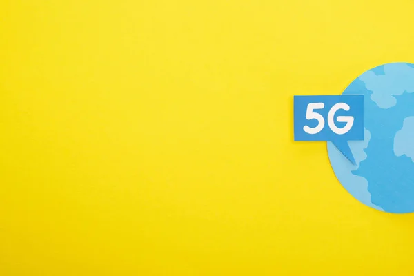 Top view of speech bubble with 5g lettering near blue globe on yellow background — стоковое фото