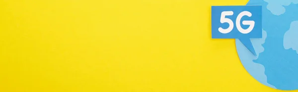 Top view of speech bubble with 5g lettering near blue globe on yellow background, panoramic shot — стоковое фото