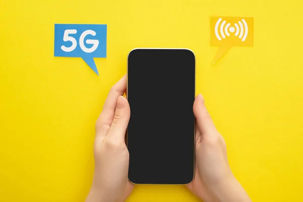 Vista cortada de mulher segurando smartphone perto de bolhas de fala com letras 5g no fundo amarelo — Fotografia de Stock