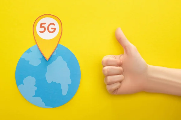 Top view of globe and 5g lettering in location mark near thumb up on yellow background — Stock Photo