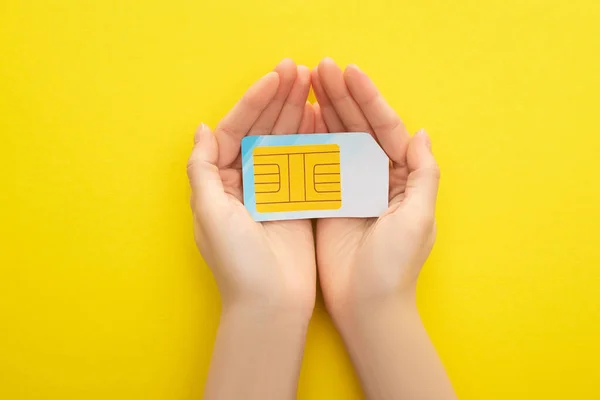 Vista cortada da mulher segurando cartão SIM no fundo amarelo — Fotografia de Stock