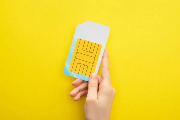 Vue recadrée de la femme tenant la carte SIM sur fond jaune — Photo de stock