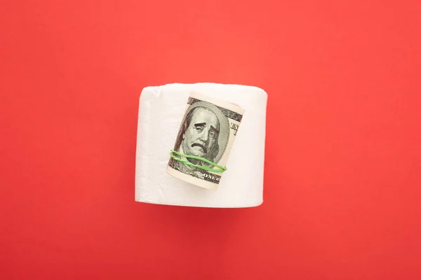 Vista superior de papel higiénico blanco con rollo de dinero sobre fondo rojo - foto de stock
