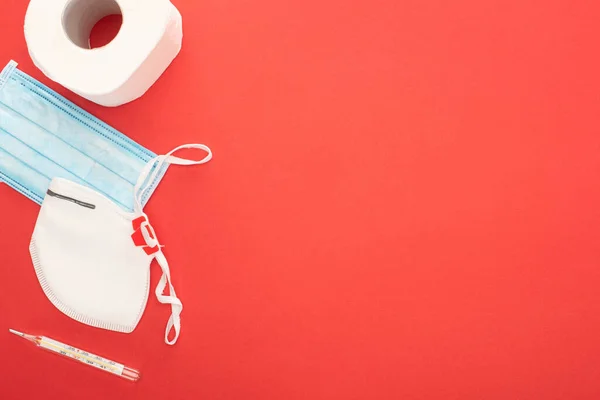 Top view of white toilet paper, safety and medical masks and thermometer on red background — Stock Photo