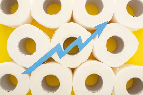 Top view of blue arrow on white toilet paper rolls on yellow background — Stock Photo