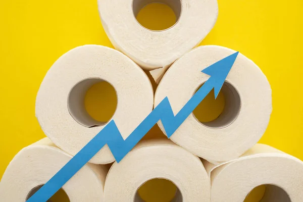 Top view of blue arrow on white toilet paper rolls on yellow background — Stock Photo