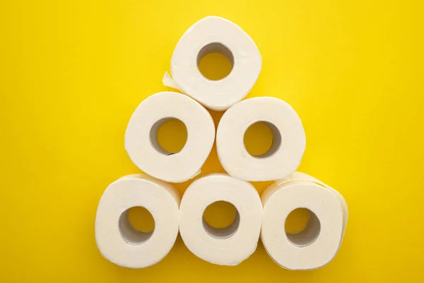 Vue du dessus des rouleaux de papier hygiénique blanc disposés en pyramide sur fond jaune — Photo de stock