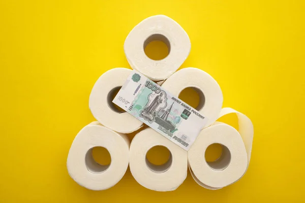 Vista superior de rollos de papel higiénico blanco dispuestos en pirámide con dinero ruso sobre fondo amarillo - foto de stock