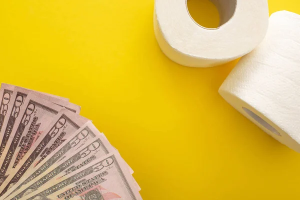 Vista dall'alto di rotoli di carta igienica bianca e dollari su sfondo giallo — Foto stock