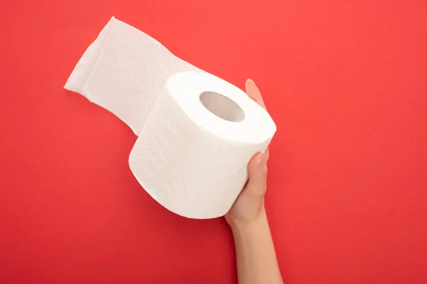 Cropped view of woman holding white toilet paper roll on red background — Stock Photo