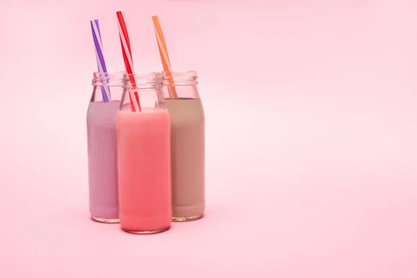 Botellas de batidos de bayas, fresas y chocolate con pajitas para beber sobre fondo rosa - foto de stock