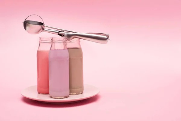 Flaschen mit Beeren, Erdbeeren und Schokolade Milchshakes mit Schöpflöffel auf Teller auf rosa Hintergrund — Stockfoto