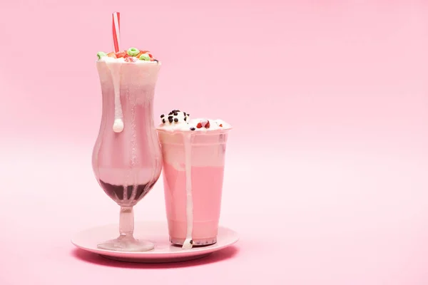 Disposable cup and glass of strawberry milkshakes on plate on pink background — Stock Photo