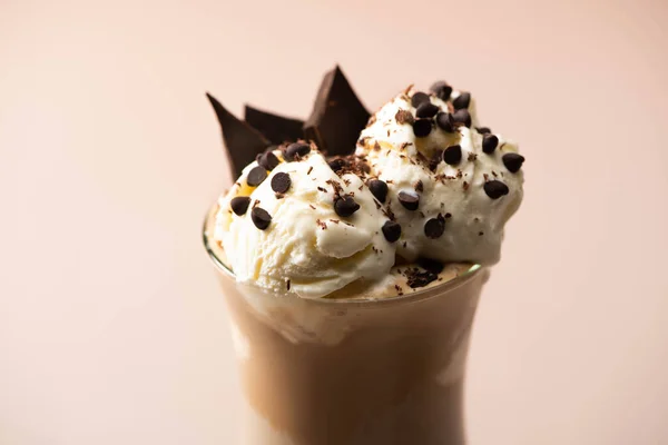 Glass of milkshake with ice cream, pieces of chocolate and candies on beige background — Stock Photo