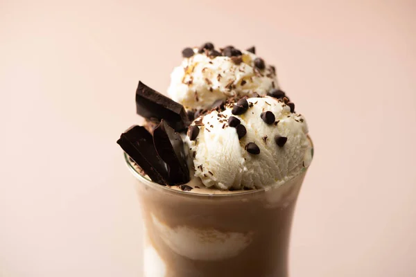 Glass of milkshake with ice cream, pieces of chocolate and candies on beige — Stock Photo