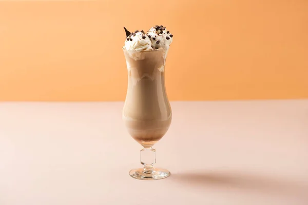 Glass of milkshake with ice cream and chocolate morsels on beige and orange — Stock Photo