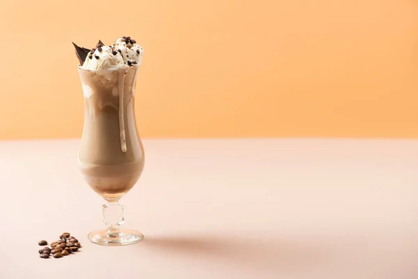 Verre de milkshake avec crème glacée et morceaux de chocolat près des grains de café sur beige et orange — Photo de stock