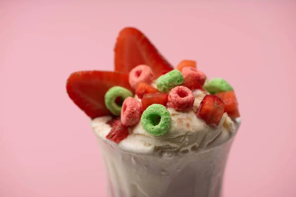 Selective focus of glass of milkshake with ice cream, cut strawberries and candies isolated on pink — Stock Photo