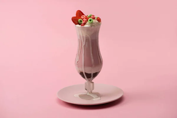 Стакан вкусного молочного коктейля с конфетами и клубникой на тарелке на розовом фоне — стоковое фото