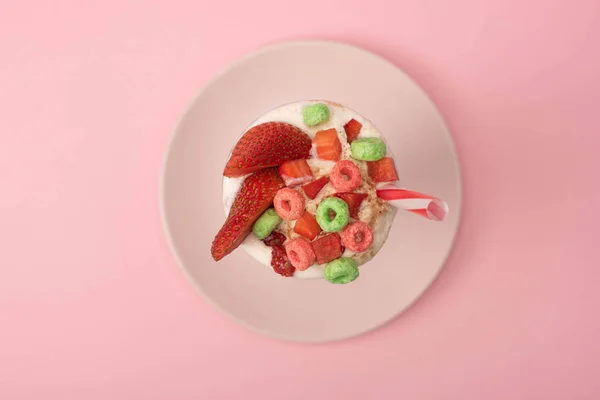 Top view of milkshake with drinking tube, strawberry halves and candies on plate on pink background — Stock Photo