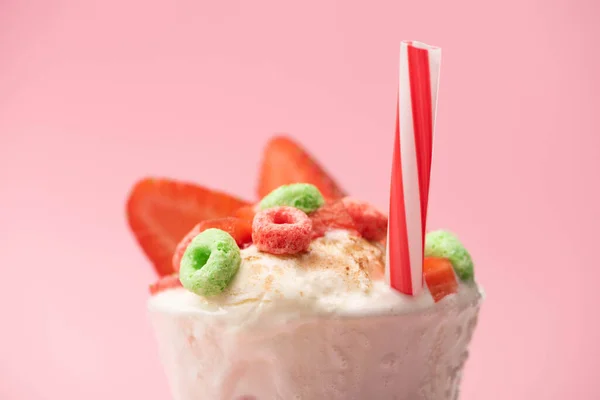 Selective focus of glass of milkshake with ice cream, strawberry halves, candies and drinking straw on pink background — Stock Photo