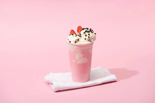 Einwegbecher Milchshake mit Schokoladenstücken und Erdbeerhälften auf Servietten auf rosa Hintergrund — Stockfoto