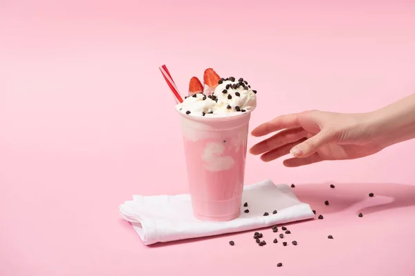 Vue partielle de la main féminine avec tasse jetable de milkshake avec des morceaux de chocolat et fraise sur des serviettes sur rose — Photo de stock