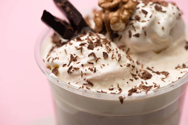 Селективный фокус одноразовой чашки молочного коктейля с мороженым, грецким орехом, шоколадной стружкой и кусочками на розовом — стоковое фото