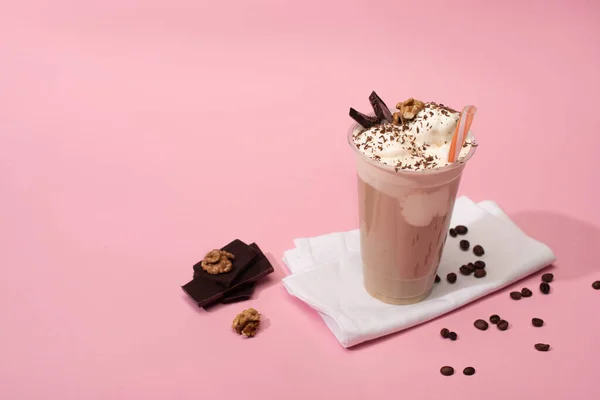 High angle view of disposable cup of milkshake with walnuts, chocolate pieces and coffee grains on napkins on pink — Stock Photo