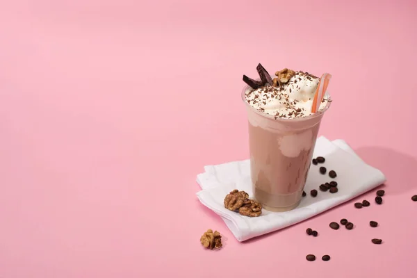 High angle view of disposable cup of chocolate milkshake with walnuts and coffee grains on napkins on pink — Stock Photo