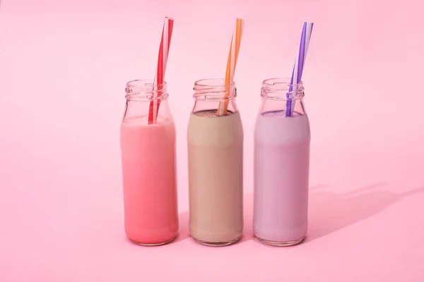 Flaschen mit Beeren, Erdbeeren und Schokolade Milchshakes mit Trinkhalmen auf rosa Hintergrund — Stockfoto