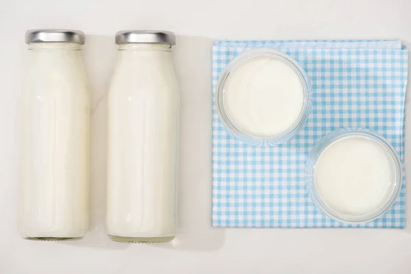Вид зверху пляшок і келихів домашнього йогурту на плетеній тканині на білому тлі — стокове фото