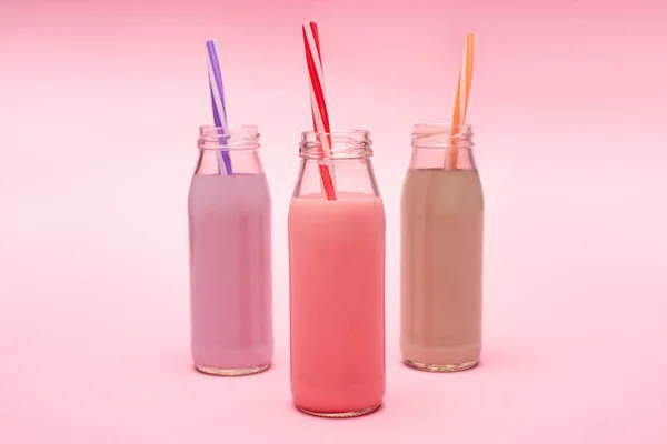 Бутылки разноцветных ягод, клубничных и шоколадных молочных коктейлей с соломинками на розовом — стоковое фото