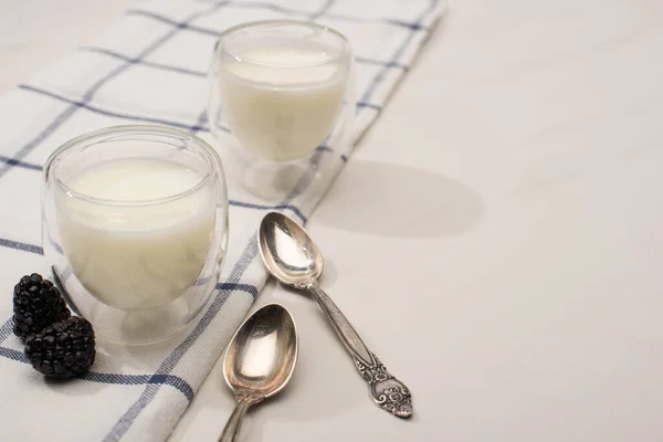 Selektiver Fokus von Gläsern hausgemachten Joghurt mit Brombeeren auf Tuch in der Nähe von Teelöffeln auf weißem Hintergrund — Stockfoto