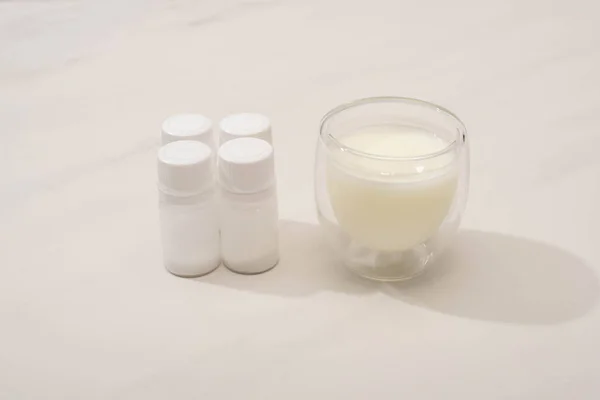 Glass of homemade yogurt near containers with starter cultures on white background — Stock Photo