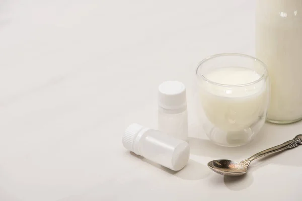 Vista de alto ângulo de garrafa e vidro de iogurte caseiro perto de recipientes com culturas iniciais e colher de chá em branco — Fotografia de Stock