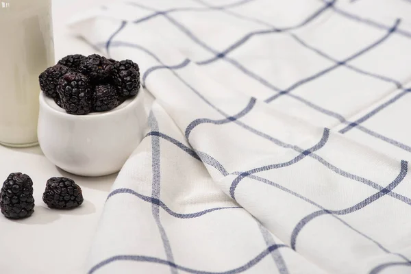 Selective focus of bottle of homemade yogurt and sugar bowl with blackberries near plaid fabric on white — Stock Photo