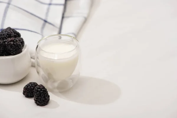 High angle view of glass of homemade yogurt and sugar bowl with blackberries near plaid fabric on white — Stock Photo