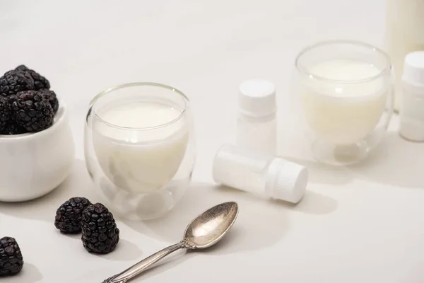 High angle view of glasses of yogurt, teaspoon, containers with starter cultures and sugar bowl with blackberries on white — Stock Photo