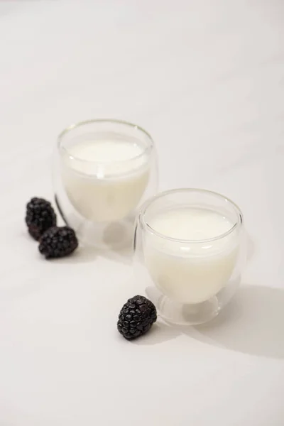 High angle view of glasses of homemade yogurt near blackberries on white background — Stock Photo
