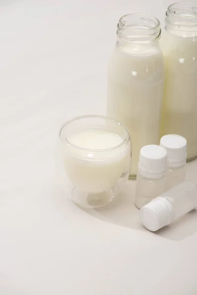 Высокий угол обзора бутылок и стакана домашнего йогурта возле контейнеров с закуски культур на белом — стоковое фото
