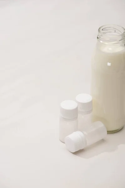 Високий кут зору пляшки домашнього йогурту біля контейнерів з початковими культурами на білому тлі — стокове фото