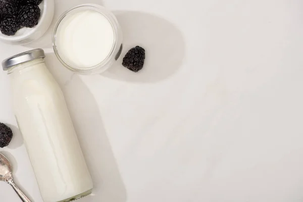 Vista superior de botella y vaso de yogur casero con moras sobre fondo blanco - foto de stock