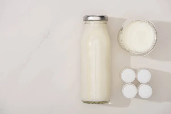 Vista superior de garrafa e vidro de iogurte caseiro perto de recipientes com culturas iniciais em fundo branco — Fotografia de Stock