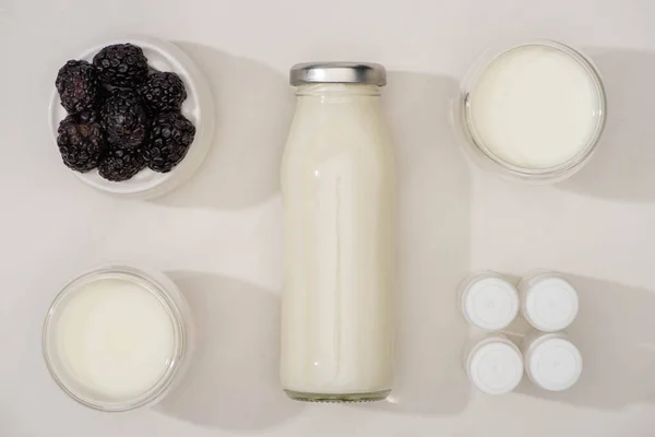 Vue du dessus de la bouteille et des verres de yaourt maison, des récipients avec des cultures d'entrée et un bol à sucre avec des mûres sur blanc — Photo de stock