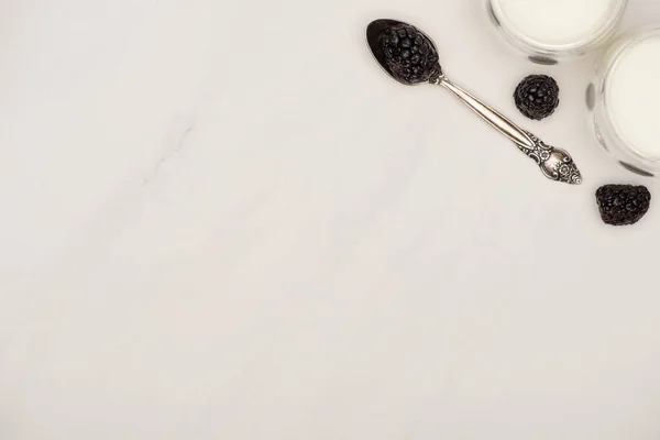 Top view of glasses of homemade yogurt and teaspoon with blackberries on white background — Stock Photo