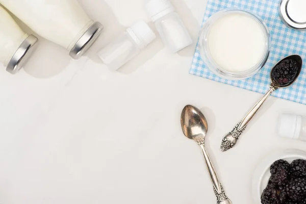 Vista dall'alto di bottiglie e bicchiere di yogurt, cucchiaini, more e contenitori con colture di antipasto su bianco — Foto stock