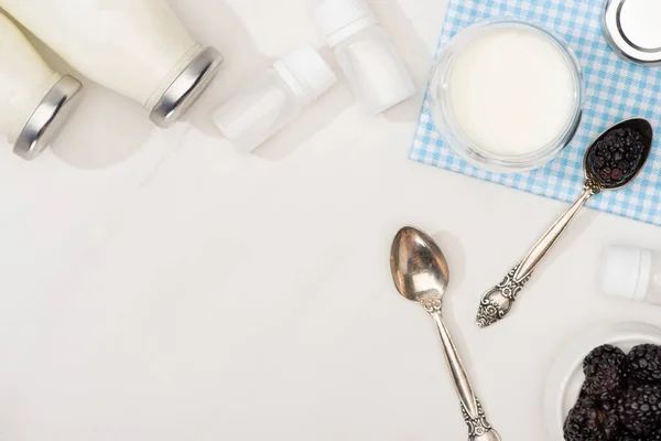 Top view of bottles and glass of yogurt, teaspoons, blackberries and containers with starter cultures on white — Stock Photo