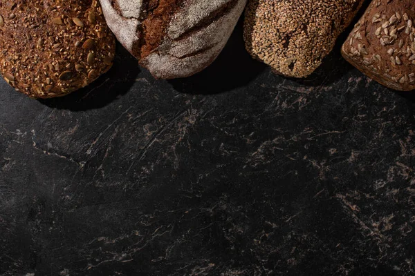 Vista superior de pão de grão inteiro cozido no forno fresco na superfície preta de pedra — Fotografia de Stock